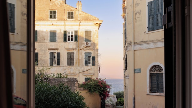 Une rue étroite, bordée de bâtiments des deux côtés, avec une vue dégagée sur la mer et une voiture rouge garée sur le côté gauche.