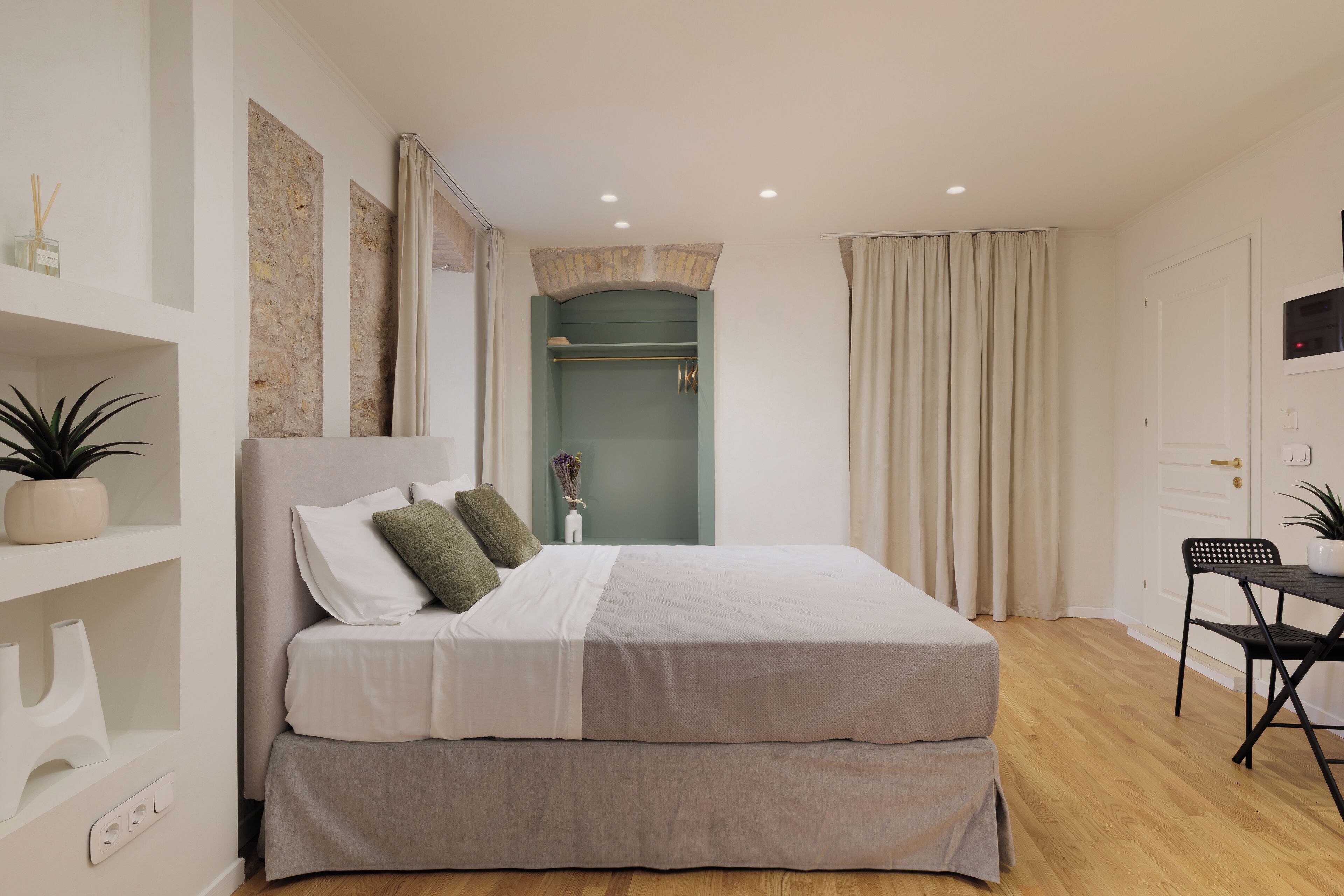 Ein modernes Schlafzimmer mit einem Bett, einem Schreibtisch und einem Stuhl. Auf dem Schreibtisch steht eine Pflanze und das Regal ist mit Dekorationen geschmückt.