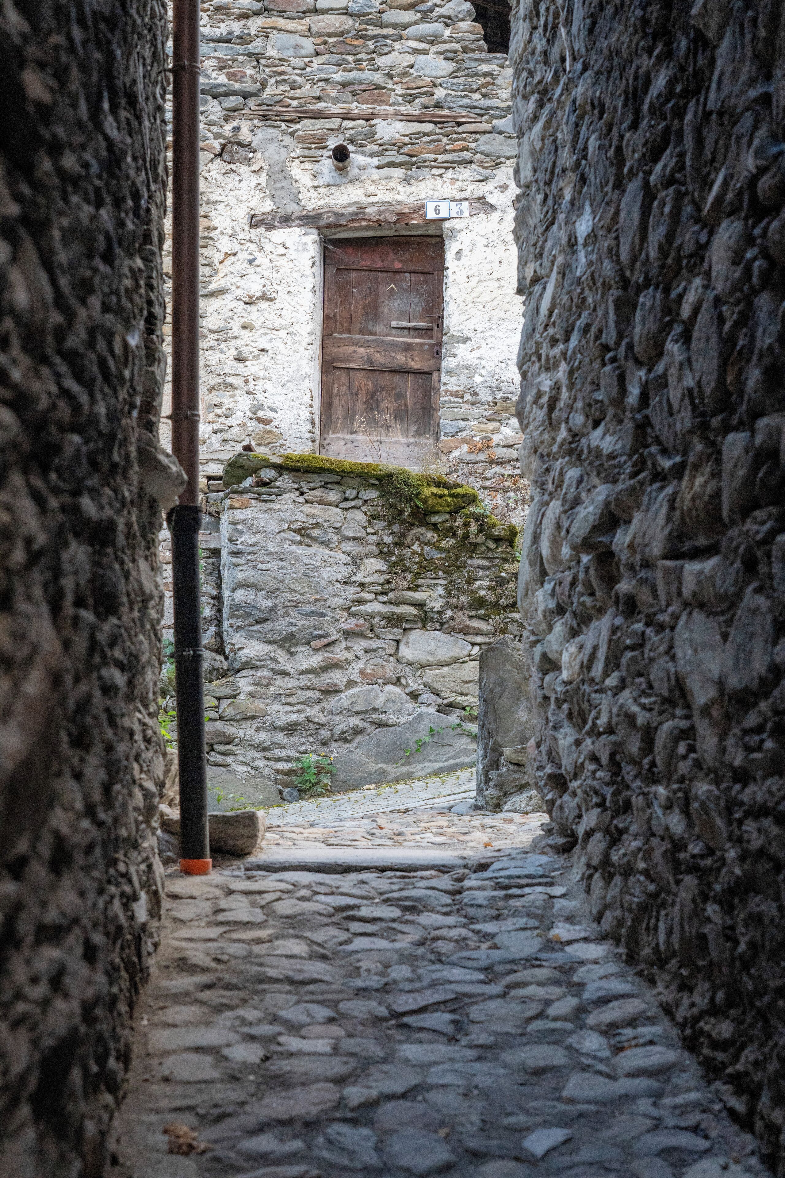Un estrecho sendero de piedra que conduce a una rústica puerta de madera, rodeado de muros de piedra.