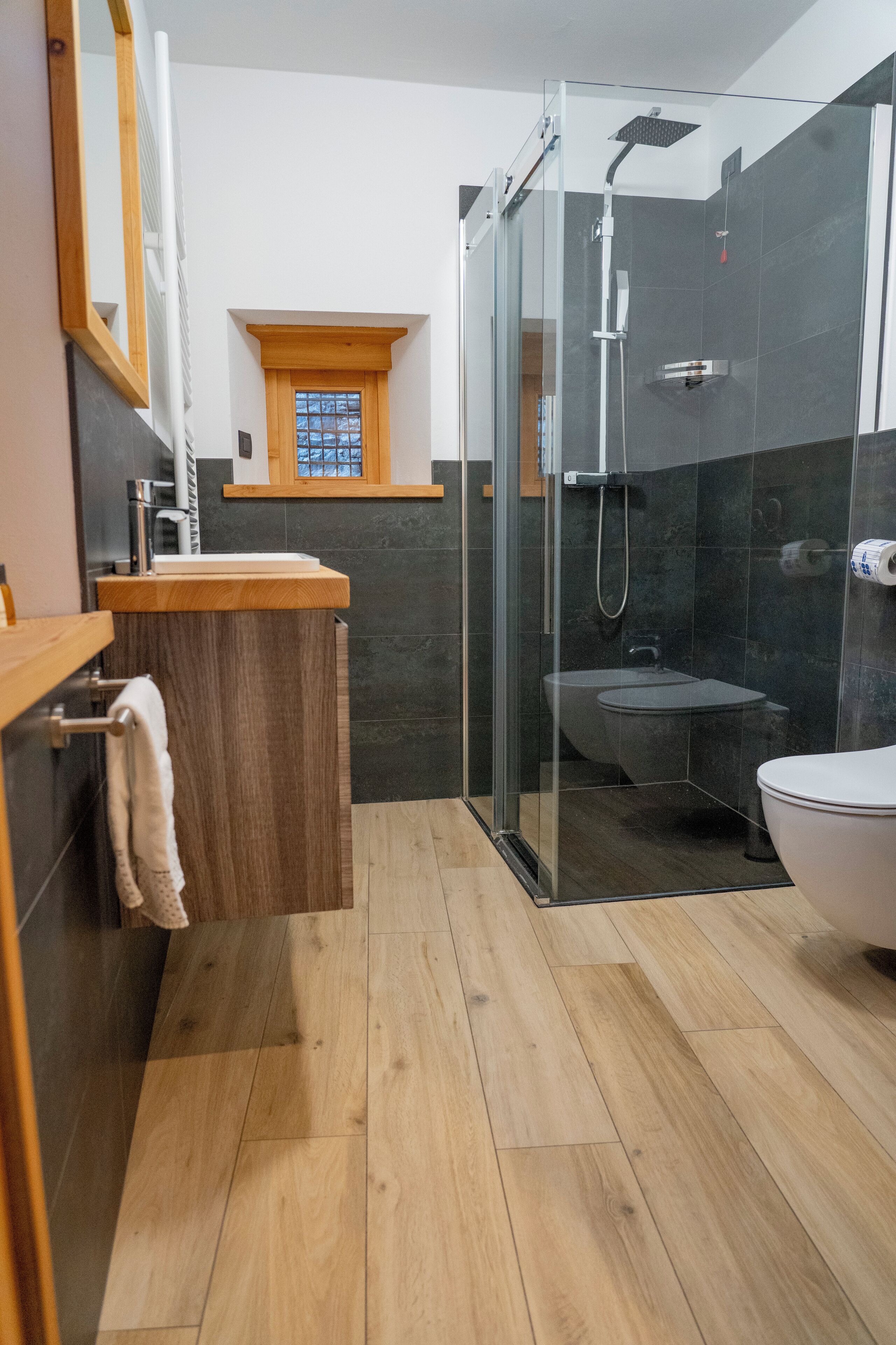 A modern bathroom with a glass-enclosed shower, a wooden vanity, and a white toilet.