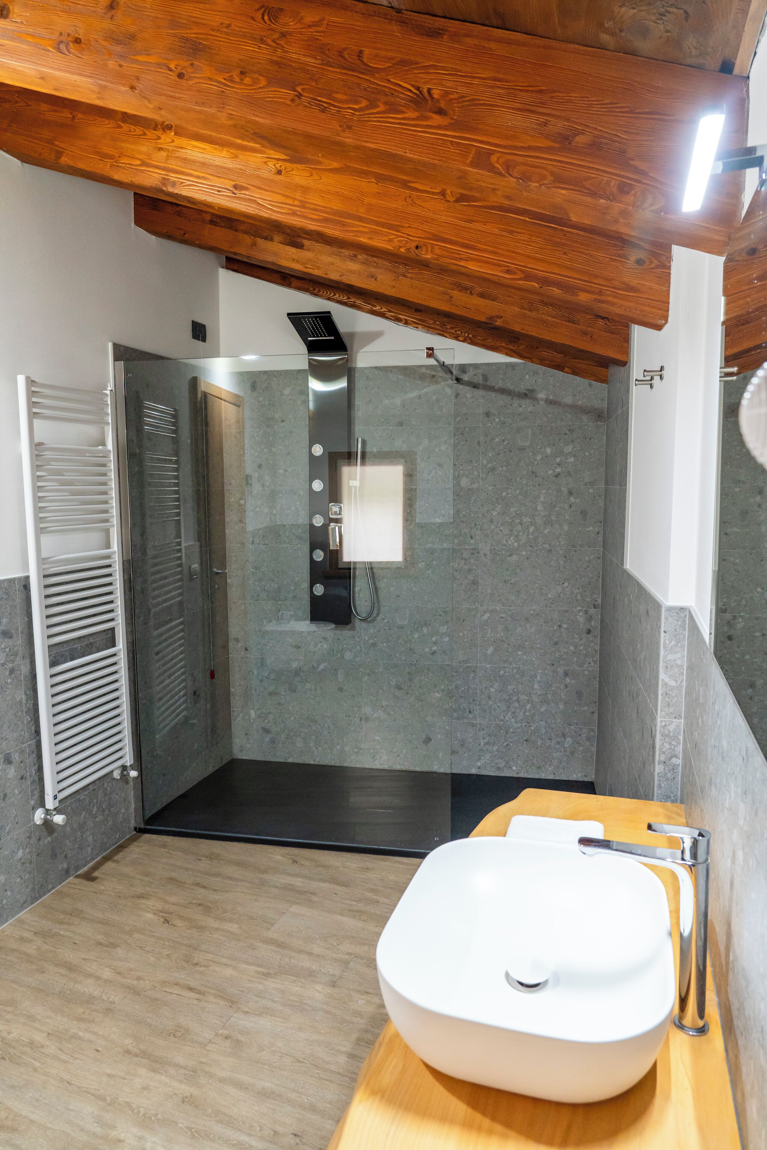 Ein modernes Badezimmer mit Holzboden, einem großen weißen Waschbecken, einer Dusche und einem Duschbereich mit Glastrennwand.