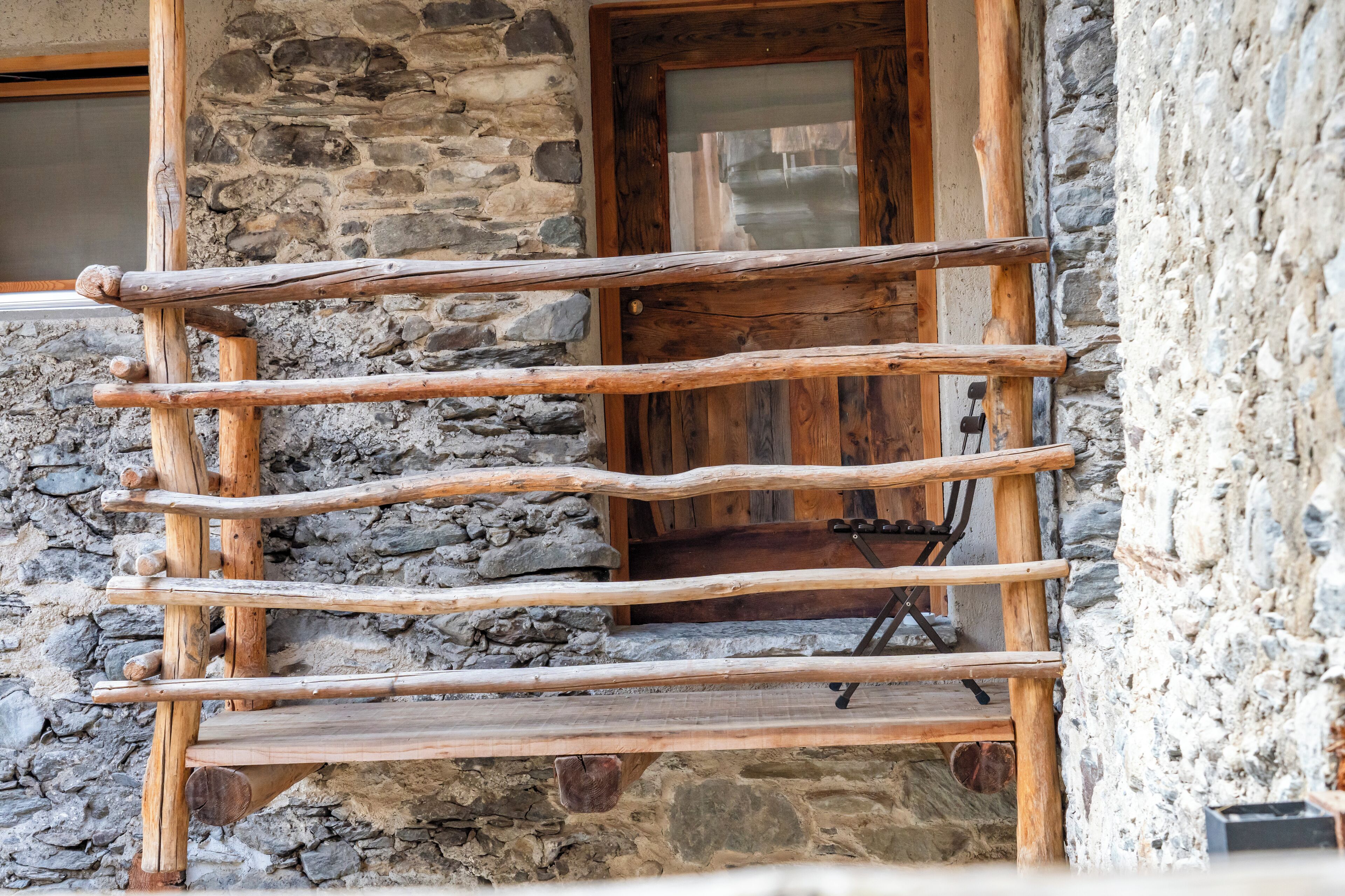 Un banco de madera con estructura metálica, ubicado frente a un edificio de piedra con puerta de madera.