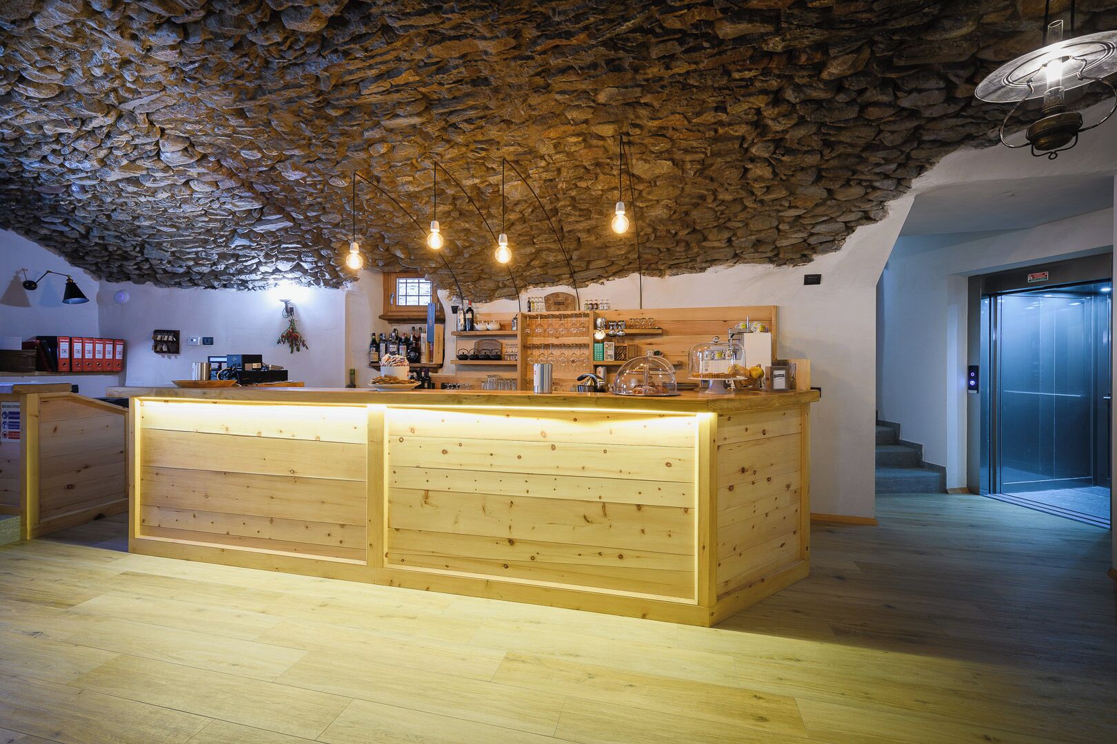 A rustic interior with a stone ceiling, wooden counter, and hanging light fixtures.