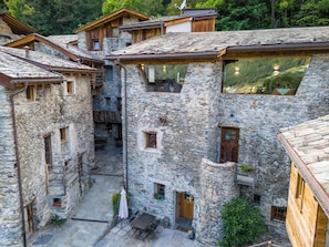 A stone building with a courtyard, wooden balconies, and a table with chairs.