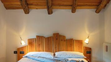 Een houten plafond met zichtbare balken, een bed met blauw beddengoed en twee wandlampen.