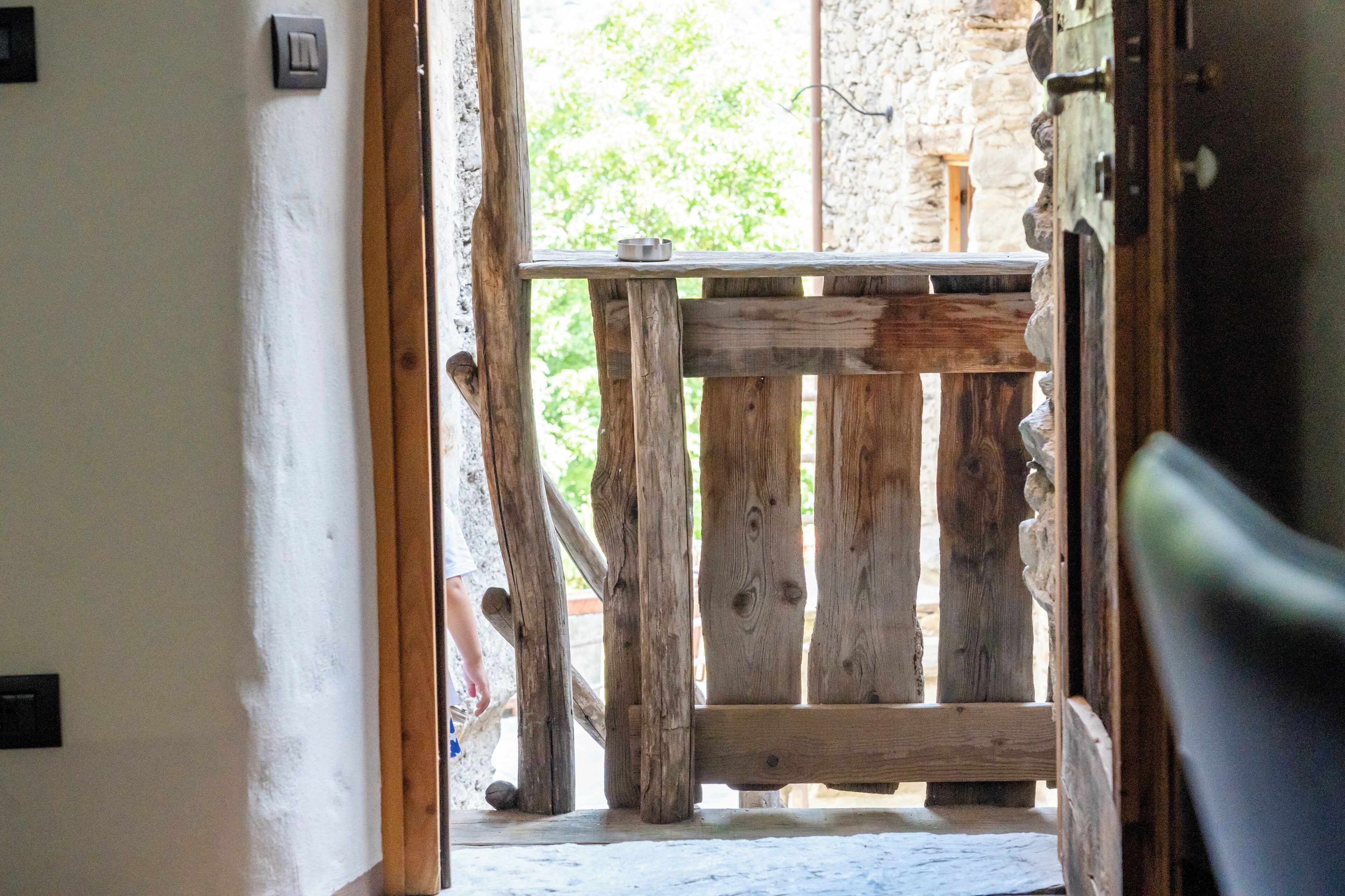 A rustic wooden bench with a metal bowl, positioned in a doorway leading to an outdoor area with greenery.