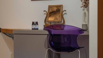 Une pièce comprenant un bureau, une chaise violette, un tableau encadré représentant un cheval, une étagère en bois et un vase contenant des fleurs séchées.