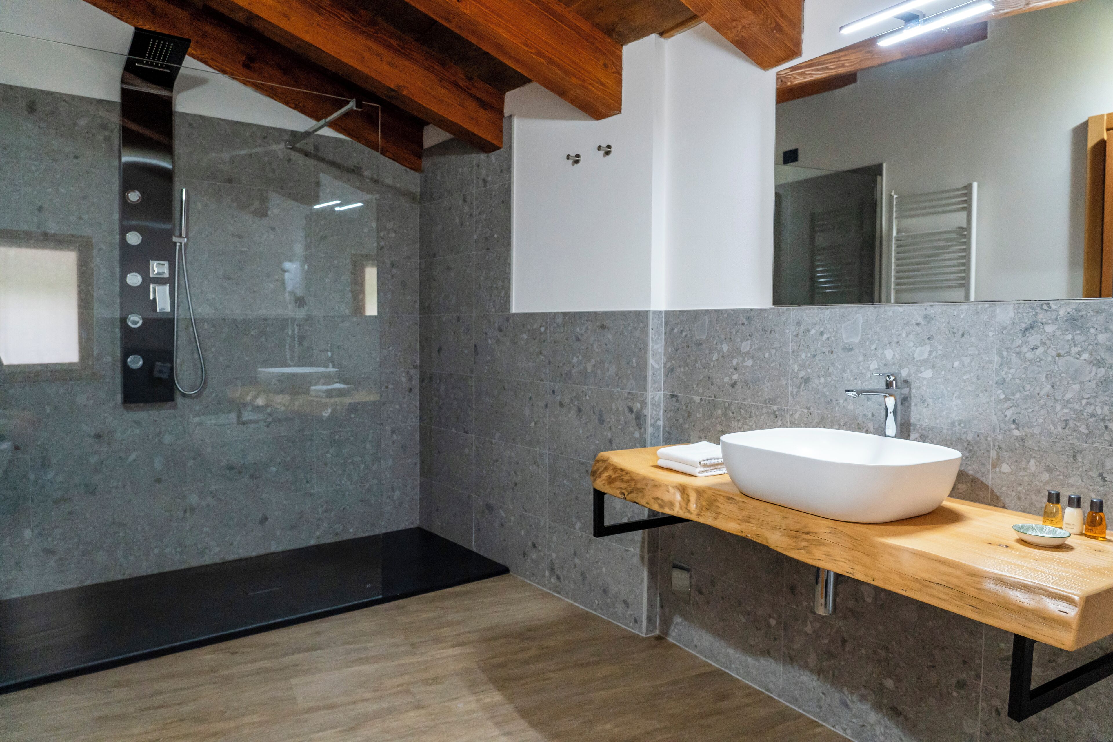 Een moderne badkamer met een vrijstaand bad, een grote spiegel en een houten wastafelmeubel met een waskom.