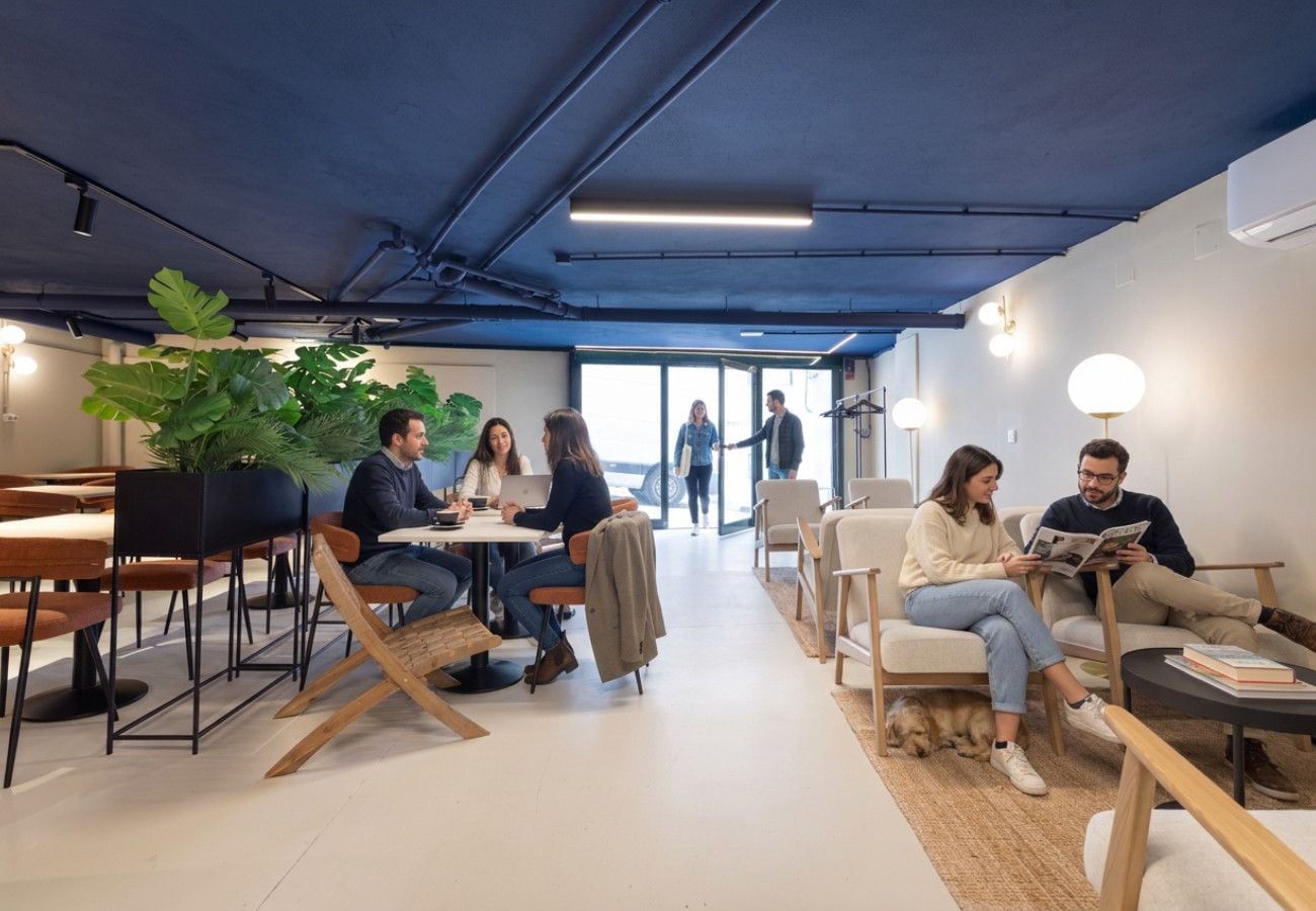 Un espacio interior moderno con mesas y sillas para comer y socializar, una planta grande en maceta y un perro.