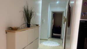Un pasillo con piso de color claro, un armario blanco con una planta encima y un refrigerador a la derecha.