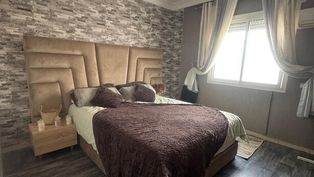 Un dormitorio con una cama grande, una mesita de noche, una lámpara decorativa y una ventana con cortinas.