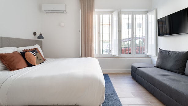 Un dormitorio con cama, sofá, televisión y ventana con cortinas.