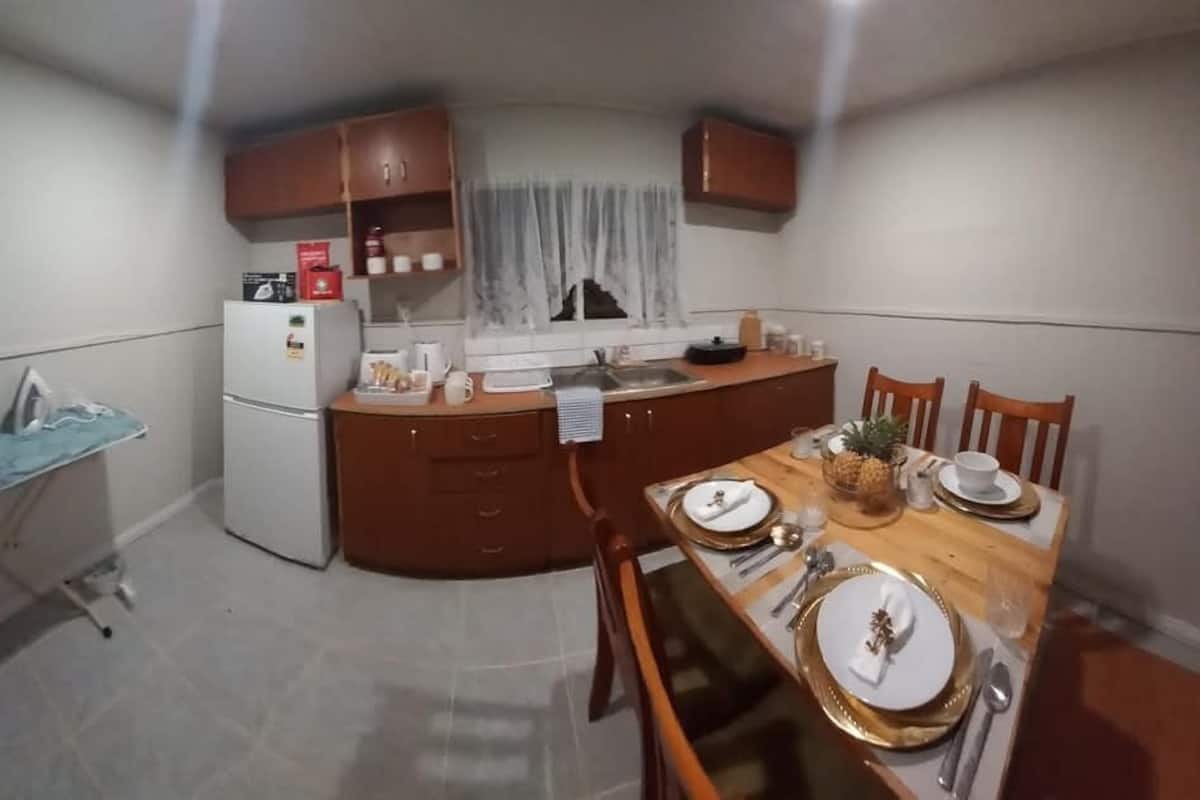 A compact kitchen with a refrigerator, microwave, and wooden cabinets. A dining table with plates and cutlery is set for four.