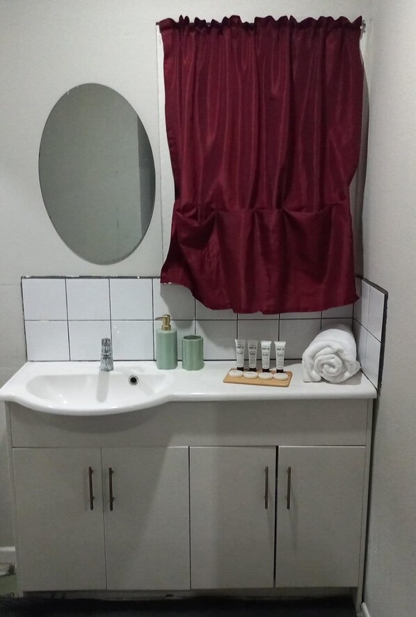 A bathroom with a white sink, a mirror, a red shower curtain, and toiletries on the counter. - Liu guesthouse (Nuku'alofa)