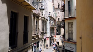 Une rue étroite bordée de bâtiments des deux côtés, avec le clocher d’une église en arrière-plan, et des gens qui se promènent.