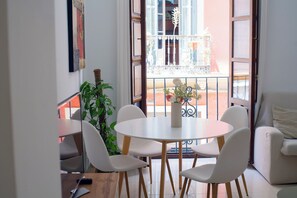 A dining area with a round table and four chairs, a potted plant, and a view of a balcony with a railing and a building in the background. - El Marqués San Juan 1 (Málaga)
