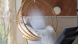 Una habitación con una silla colgante, una cama y una ventana con cortinas.