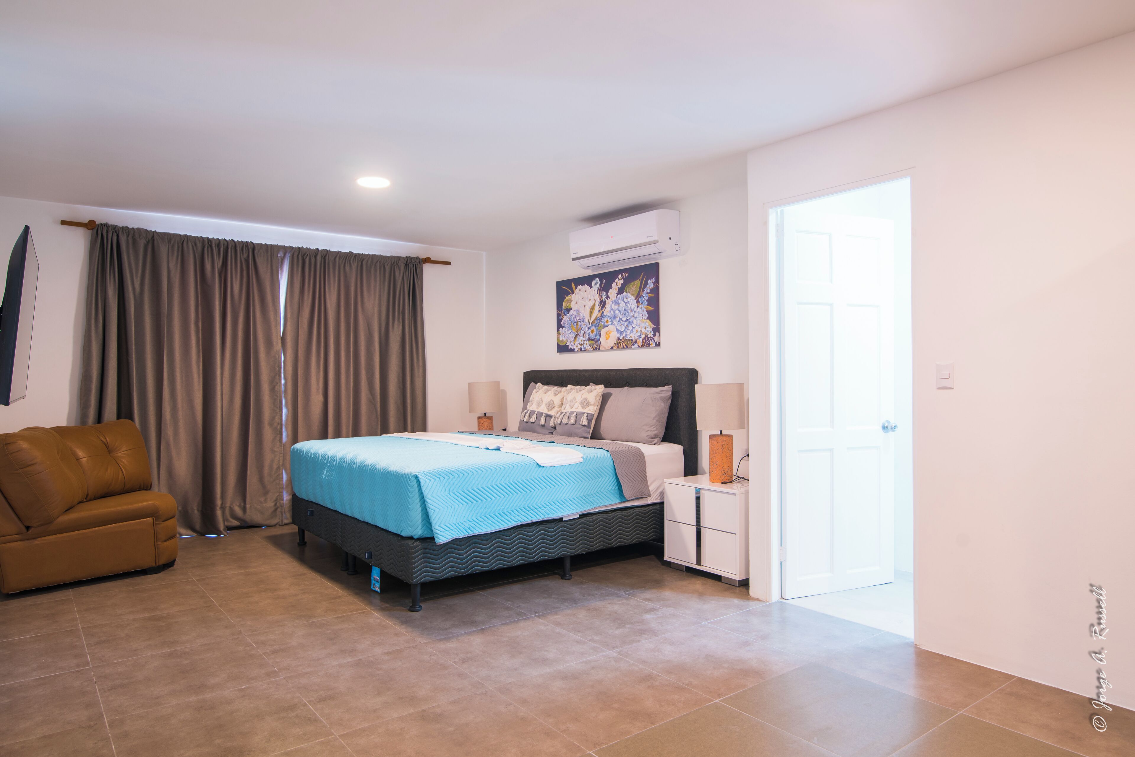A bedroom with a bed, a nightstand, a brown leather chair, and a door leading to another room.