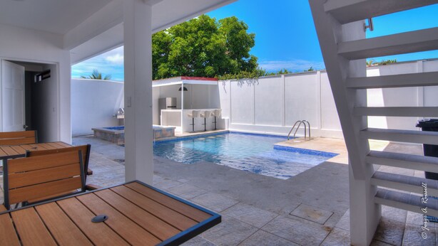 Un espace piscine extérieur moderne, doté d’une terrasse en bois, d’un mur blanc et d’un ciel d’un bleu limpide.