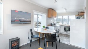 A modern kitchen with a dining area, a television mounted on the wall, and a view of the city through large windows.