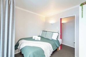 A bedroom with a bed, pillows, a blanket, a wall-mounted light, and a door.