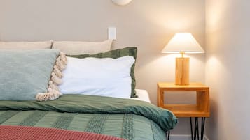 A neatly made bed with a green and white duvet, a wooden bedside table with a lamp, and a wall-mounted light fixture.