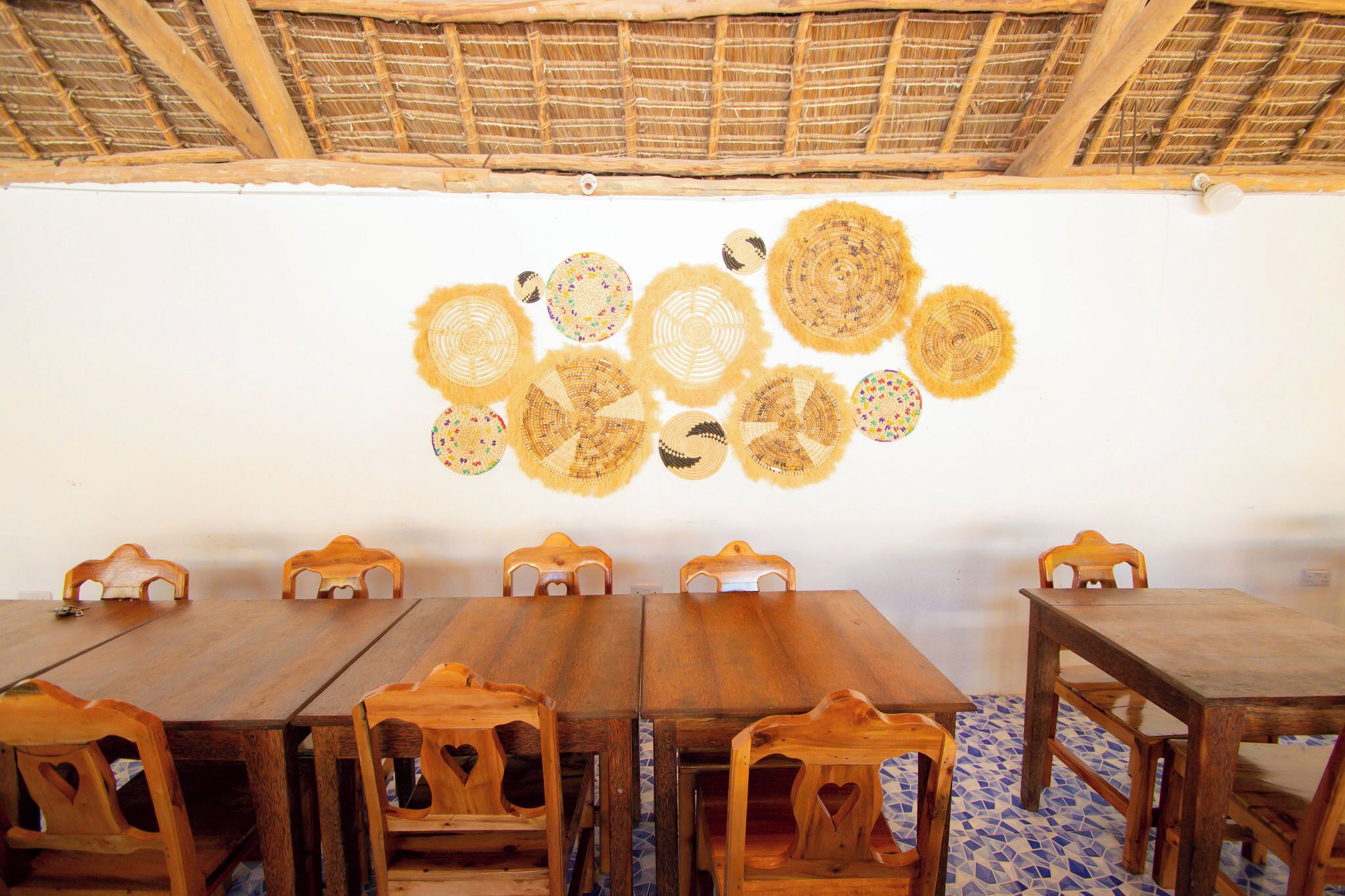 A dining area with a wooden table and chairs, a thatched roof, and woven wall decorations.