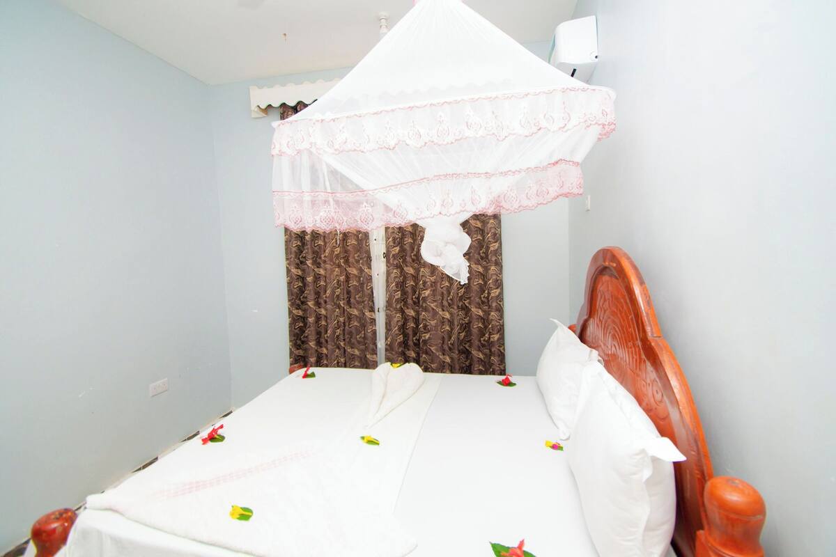 A single bed with a wooden headboard, a white canopy, and brown patterned curtains.