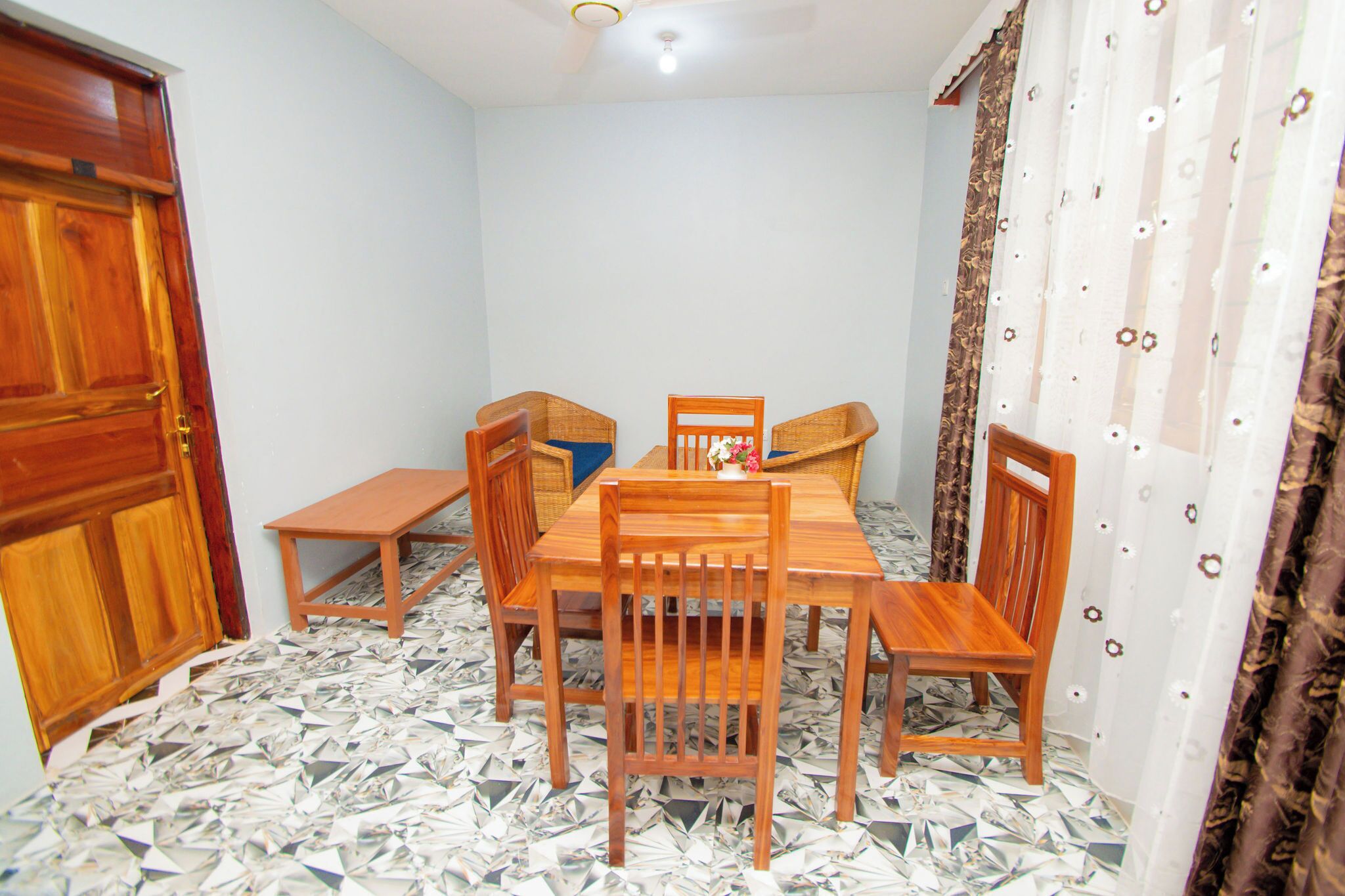 A dining area with a wooden table and chairs, a small bench, and a patterned floor.
