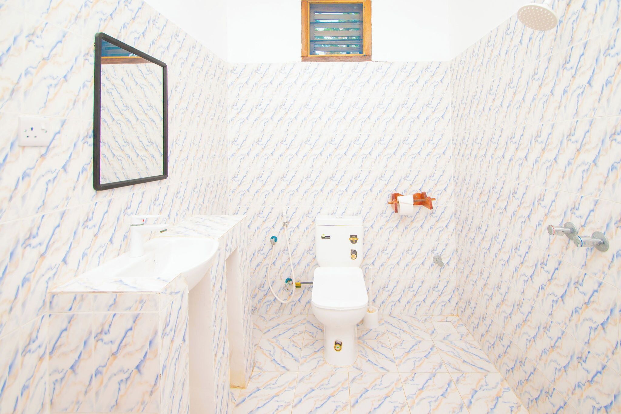 A bathroom with a marble floor, a toilet, a sink, and a shower.