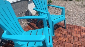 Twee turquoise Adirondack-stoelen op een houten terras voor een wit huis met een houten terras.