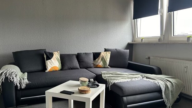 Een moderne woonkamer met een hoekbank, een kleine witte tafel en een raam met uitzicht.