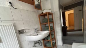 Een badkamer met een witte wastafel, houten planken, een spiegel en een groene mat.