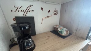 Een koffiezetapparaat op een houten aanrecht, met een muur waarop 'Kaffe' en 'praise' staan.