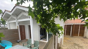 Un patio couvert avec une table et des chaises, une terrasse en bois et un jardin clôturé.