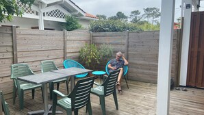 Une terrasse en bois avec une table et des chaises, une personne assise et une clôture en bois.