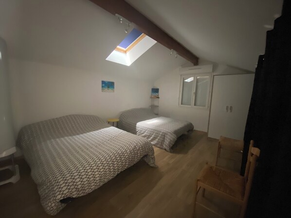 Une petite pièce bien éclairée, avec deux lits, un plancher en bois, une lucarne et une petite table.