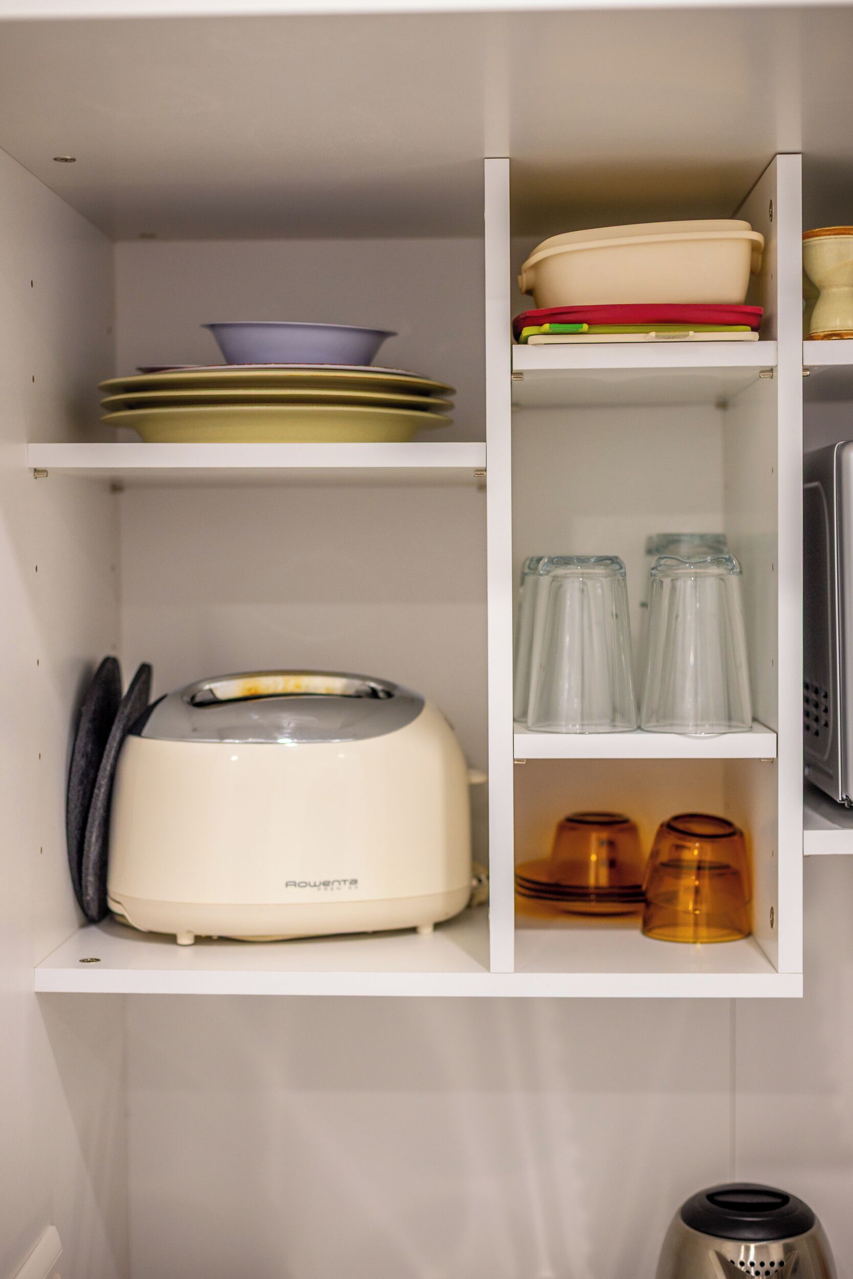 A kitchen with a toaster, shelves with dishes, and glass containers.