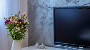 Ein modernes Wohnzimmer mit einem weißen runden Tisch, einem Blumenstrauß, einem Flachbildfernseher und einer Marmorwand.