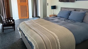 A hotel room with a large bed, a chair, a nightstand with a lamp, and a window with curtains.
