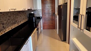A modern kitchen with white cabinets, a black countertop, a tiled backsplash, and a wooden door.