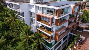 A multi-story hotel with balconies, solar panels, and a view of the sea.