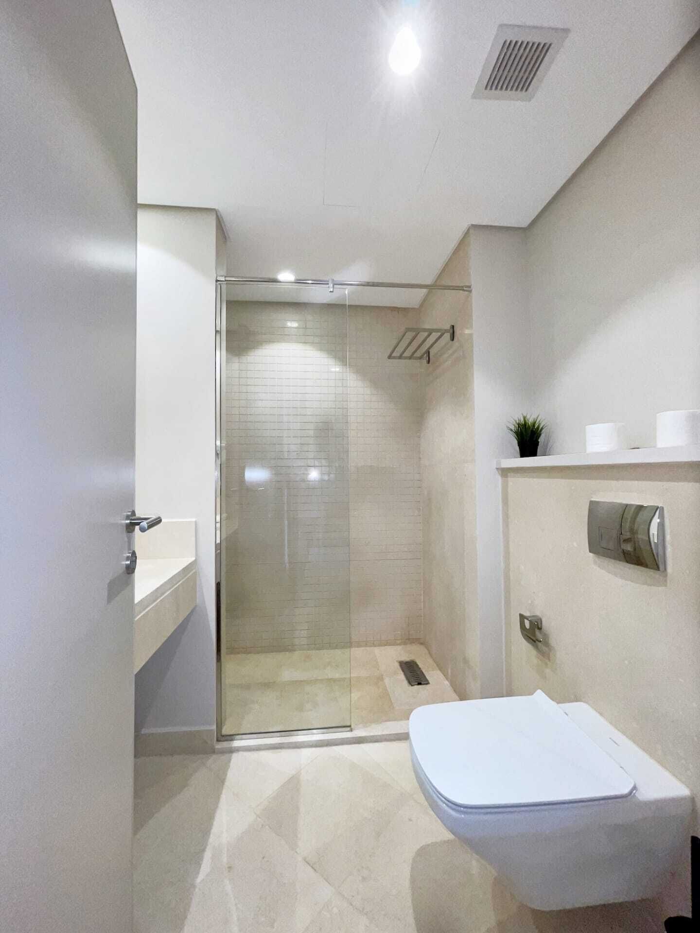 Un baño moderno con cabina de ducha de vidrio, inodoro blanco y un lavamanos pequeño.