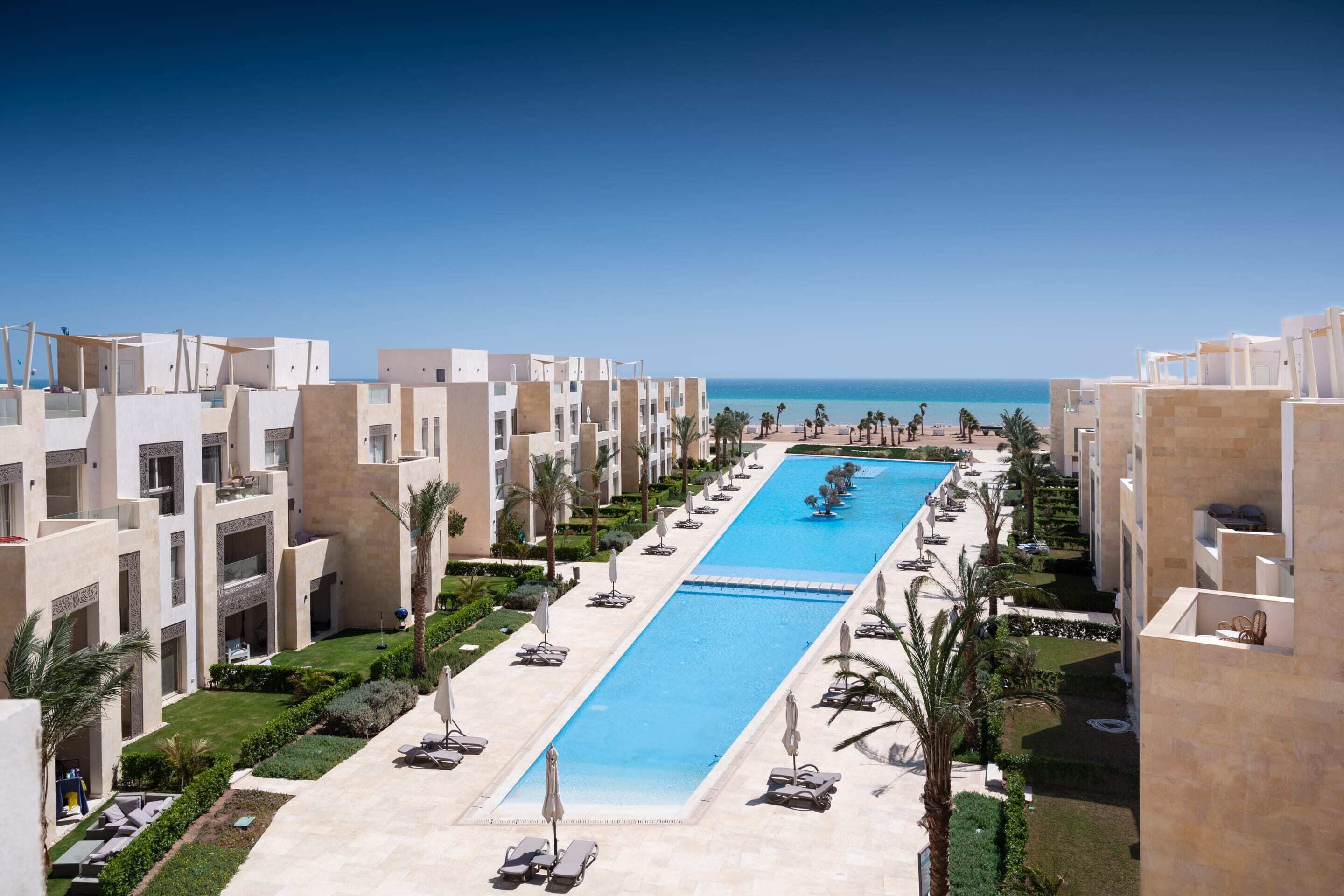 Un complexe hôtelier doté d’une longue piscine, de nombreux balcons et de palmiers.