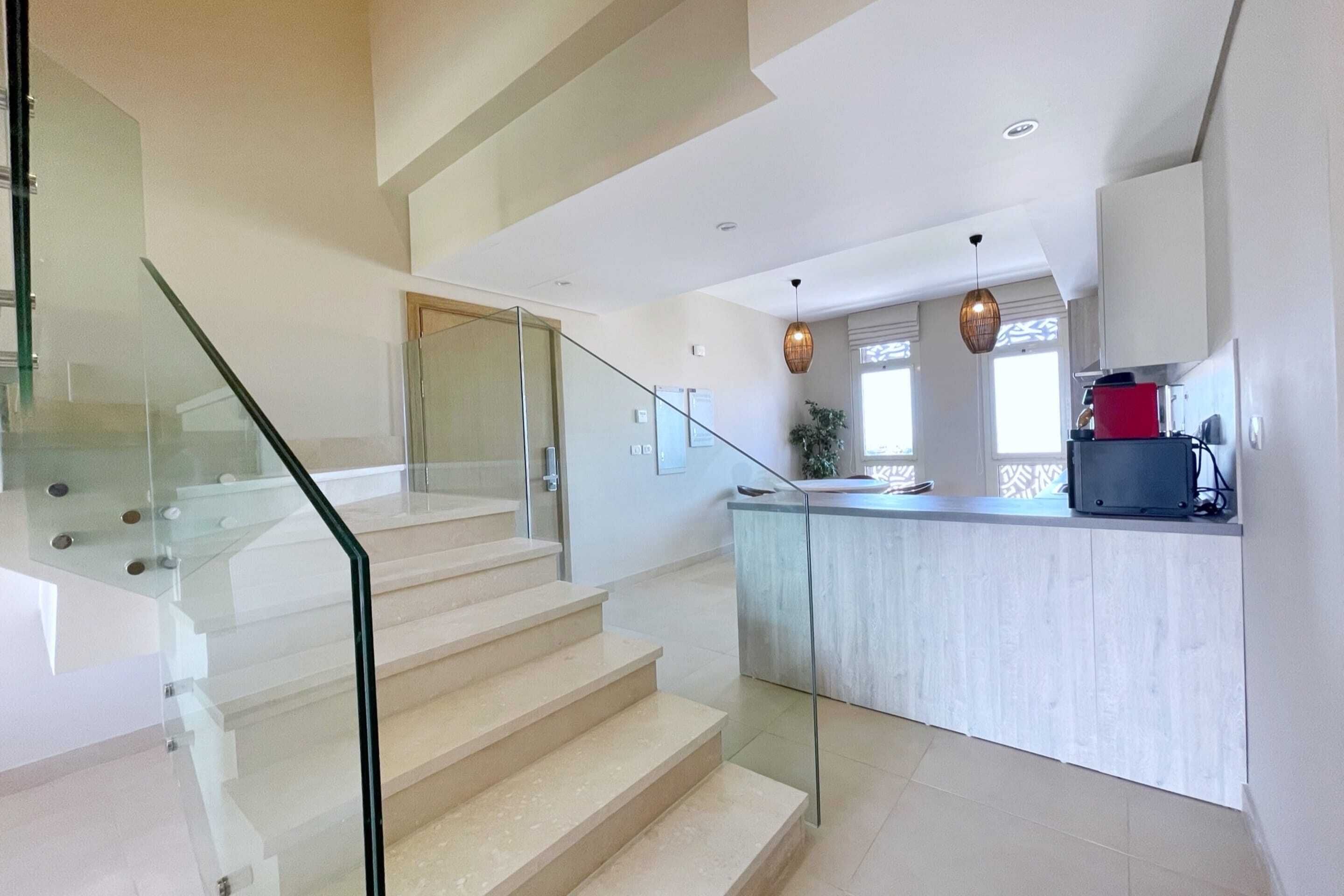 Een moderne keuken met een glazen eiland, een trap met glazen balustrades en uitzicht op de woonkamer.