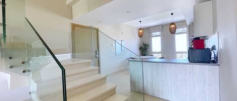 A modern kitchen with a glass island, a staircase with glass railings, and a view of the living area.