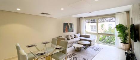 A modern living room with a glass dining table, sofas, and a large window with a view.