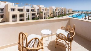 Ein Balkon mit Korbstühlen und einem kleinen Tisch, mit Blick auf einen Swimmingpool und Hotelgebäude.