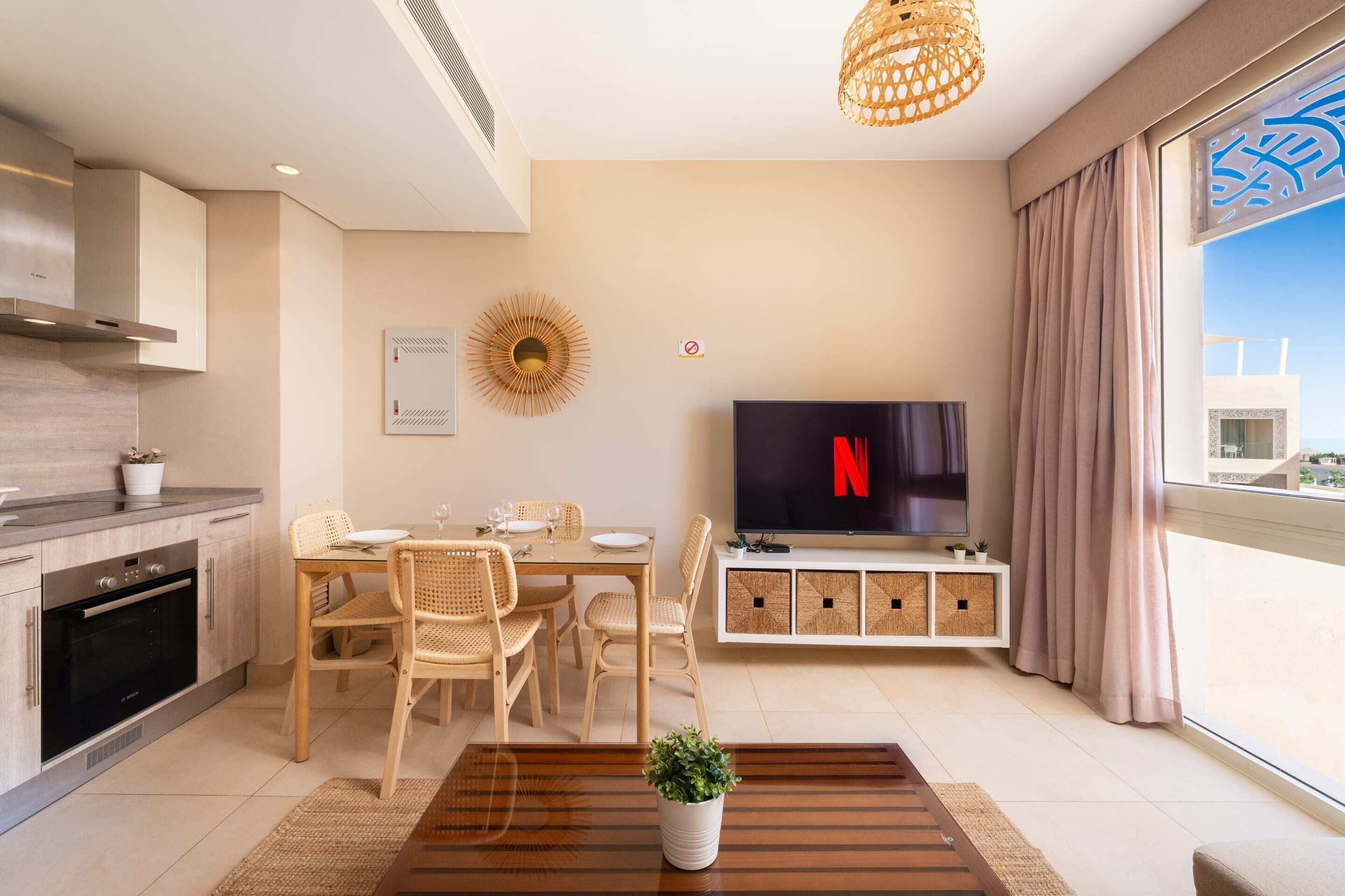 A modern living room with a dining area, a kitchen, and a large window with a view.