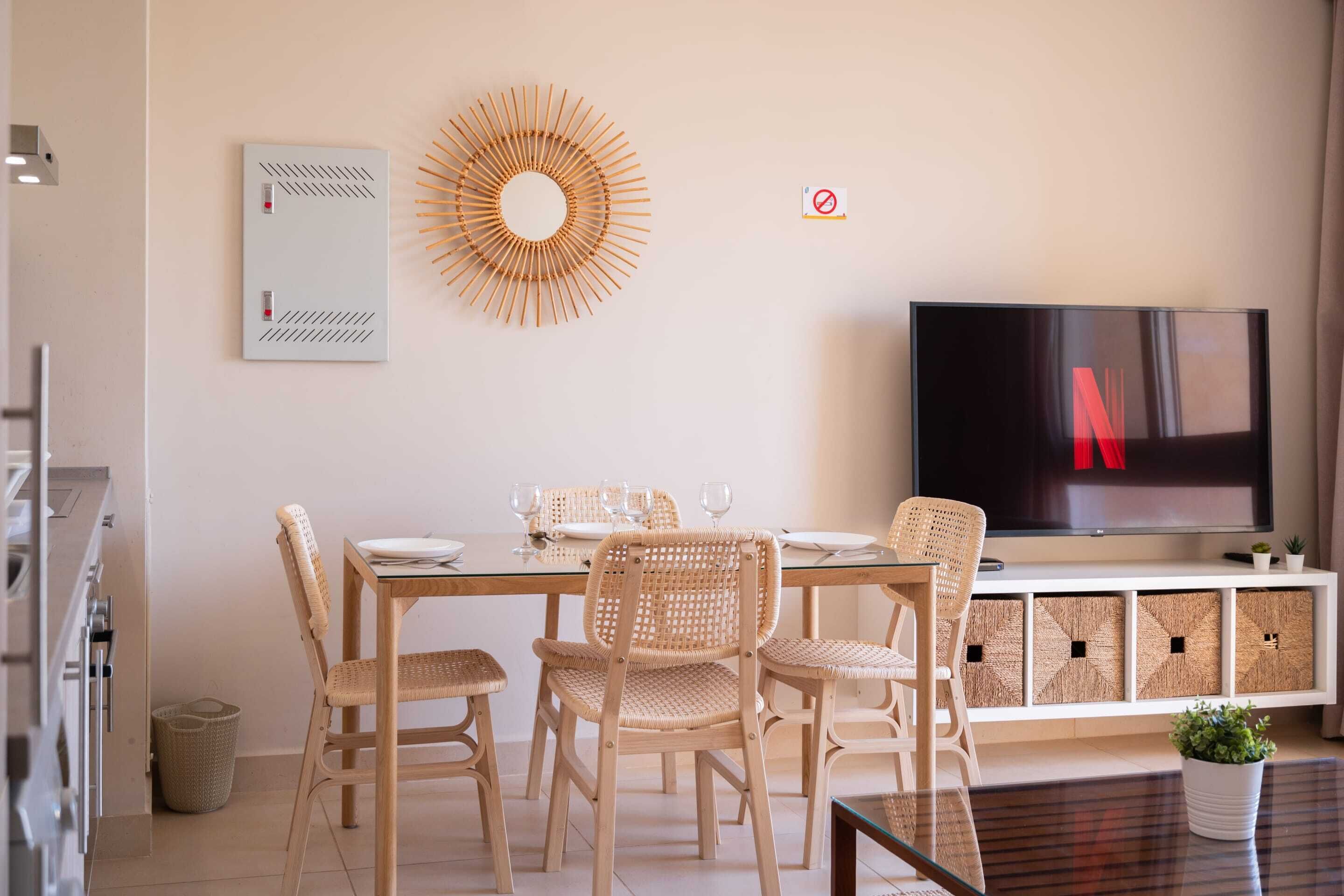 Ein modernes Wohnzimmer mit einem Glastisch, Korbstühlen, einem Fernseher und einem weißen Schrank mit Stauraum.